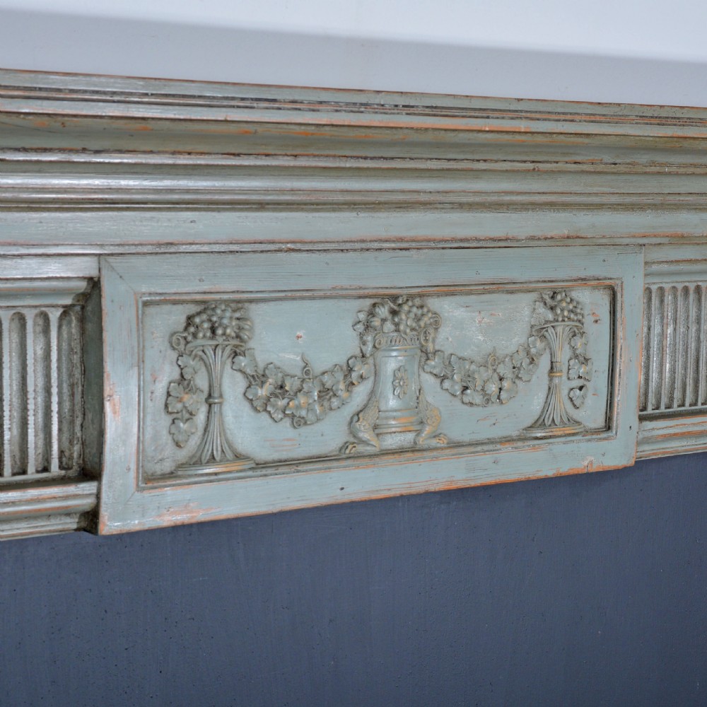 A carved Georgian Neoclassical fire surround painted pale blue, featuring fluted pilasters, decorative festoons, and a central urn panel. View VII