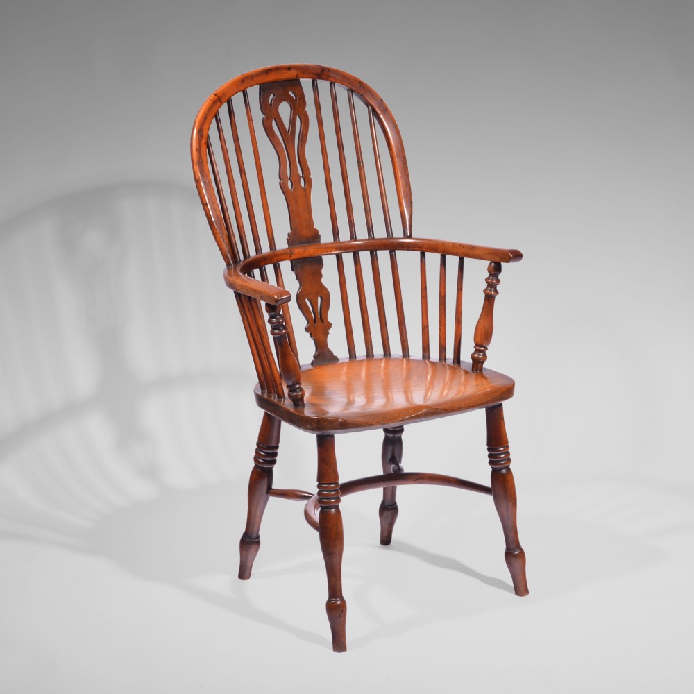 An antique yew wood highback Windsor armchair featuring a steam-bent hoop back, central pierced splat, turned spindles, carved saddle seat, and turned legs with a crinoline stretcher.