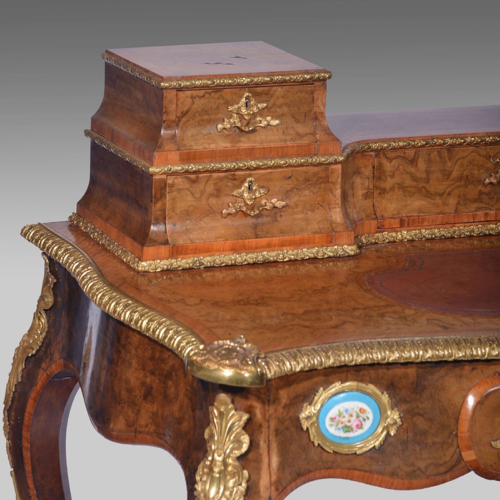 A Louis XV style walnut bureau plat desk featuring a raised superstructure of small drawers, gilt-bronze mounts, floral porcelain plaques, and cabriole legs. View V