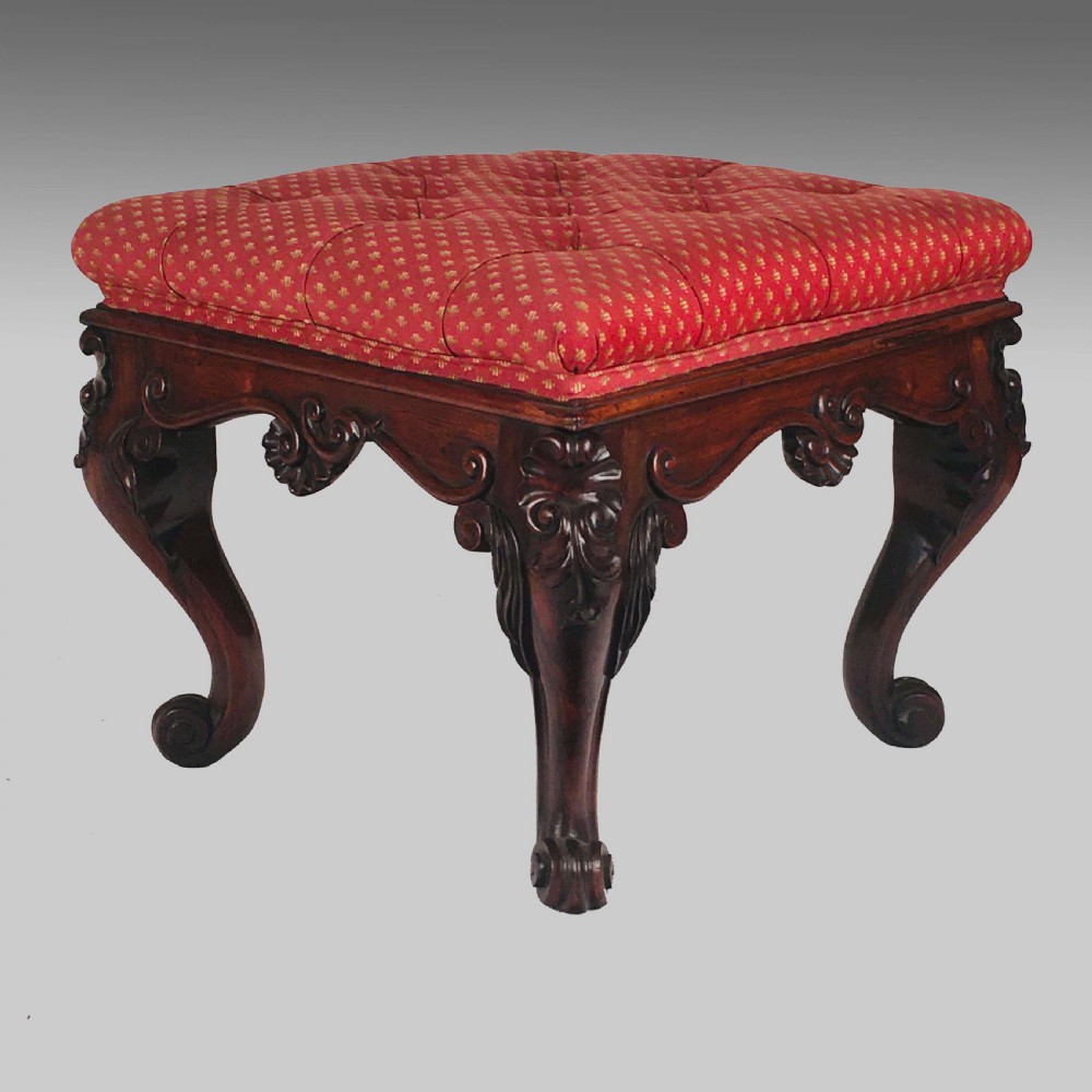 A square antique Anglo-Indian rosewood stool featuring a button-tufted red upholstery seat above intricately carved cabriole legs.