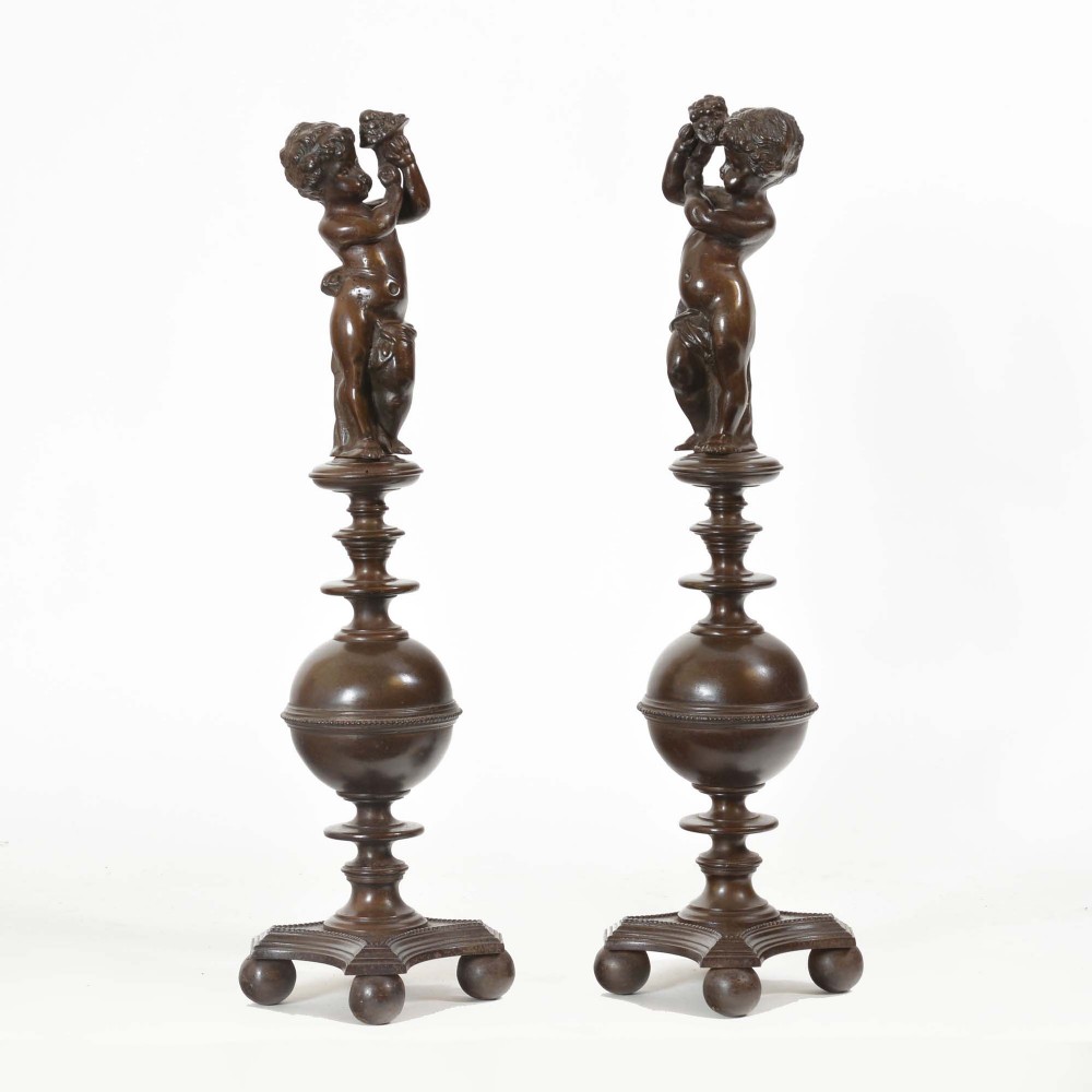 A pair of dark bronzed cast iron Renaissance Revival andirons featuring classical putti figures atop turned baluster stems and spherical knops supported by tripod ball feet.