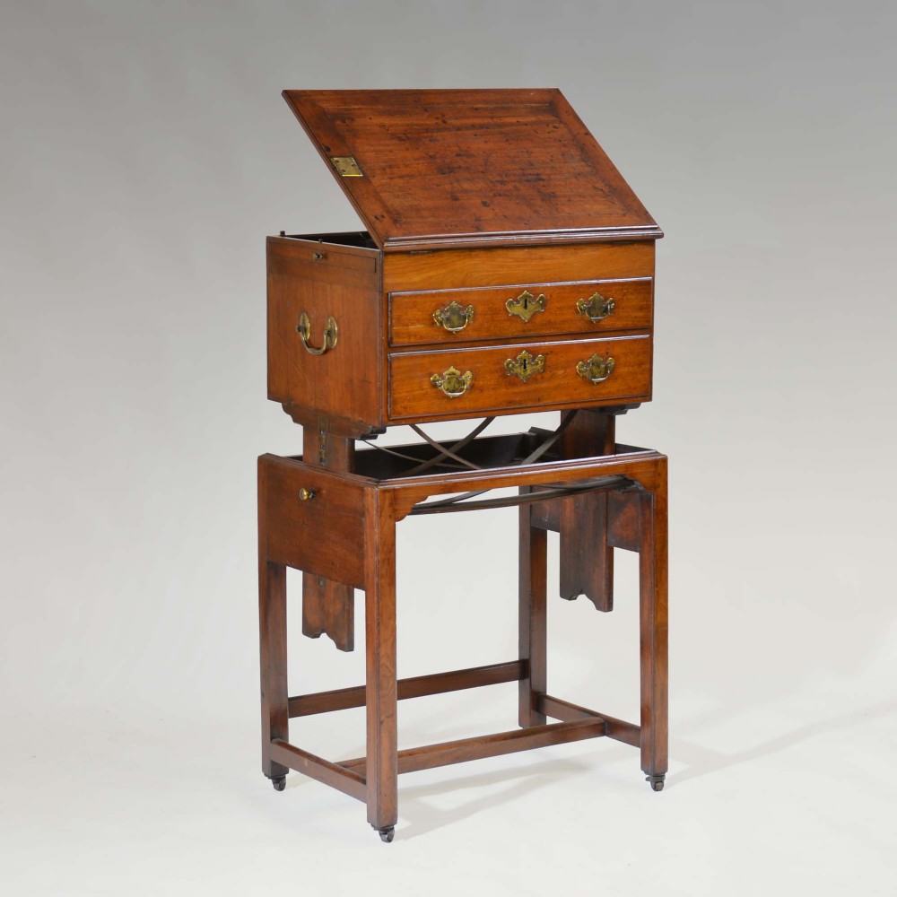 A Georgian mahogany architects desk featuring an adjustable angled writing slope, brass hardware, side carrying handles, and a base stand with castors.