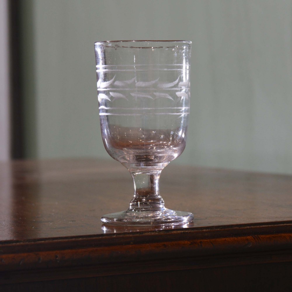 A clear 19th-century glass rummer featuring a short stem, circular foot, and wheel-engraved geometric band pattern around the bucket-shaped bowl.