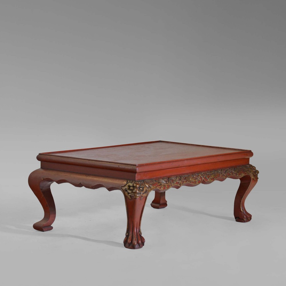 A low 19th-century Chinese red lacquer table featuring cabriole legs carved with mask knees, claw feet, and an ornate relief-carved apron.