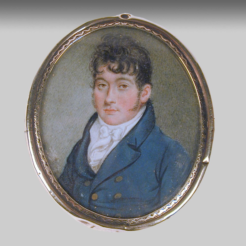 An oval Regency portrait miniature depicting a gentleman wearing a dark blue double-breasted coat and white cravat within an engraved metal frame.