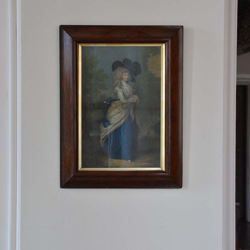 A framed portrait print depicting Georgiana, Duchess of Devonshire in a wide-brimmed feathered hat and blue gown, housed in a dark wood frame with a gilded inner border.