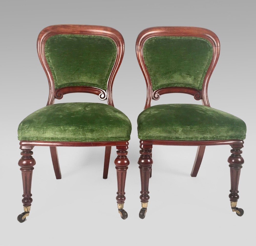 A pair of Victorian mahogany balloon back chairs upholstered in green velvet with turned front legs and brass castors.