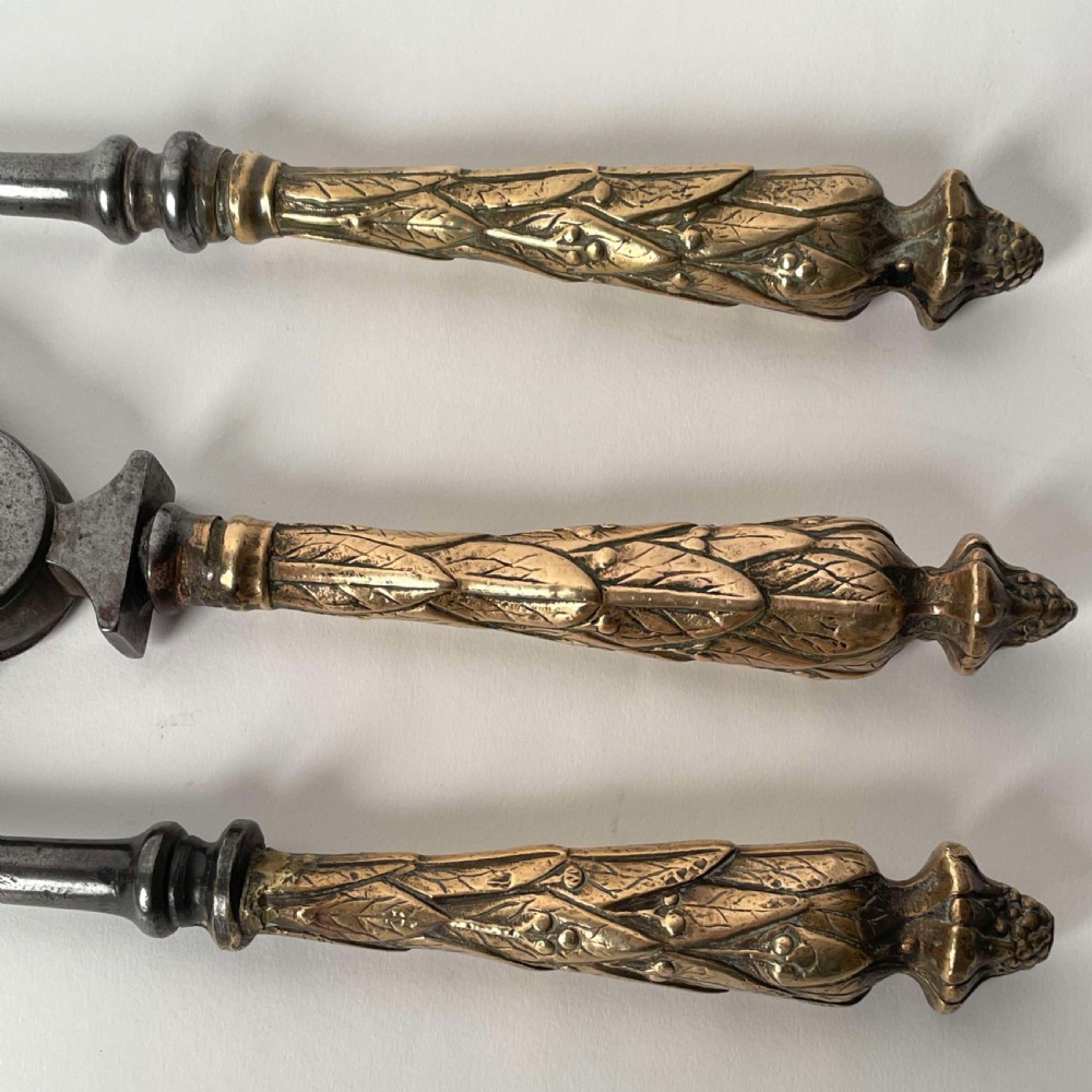 A set of three Georgian fire irons featuring steel shafts and ornate gilt brass foliate handles including a pierced shovel, tongs, and poker. View II