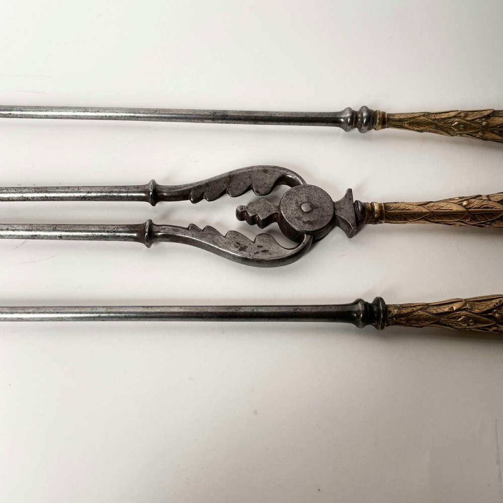 A set of three Georgian fire irons featuring steel shafts and ornate gilt brass foliate handles including a pierced shovel, tongs, and poker. View V