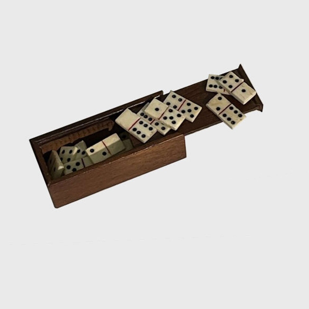 A miniature set of cream bone domino tiles spilling out from a rectangular dark wood box with a sliding lid.