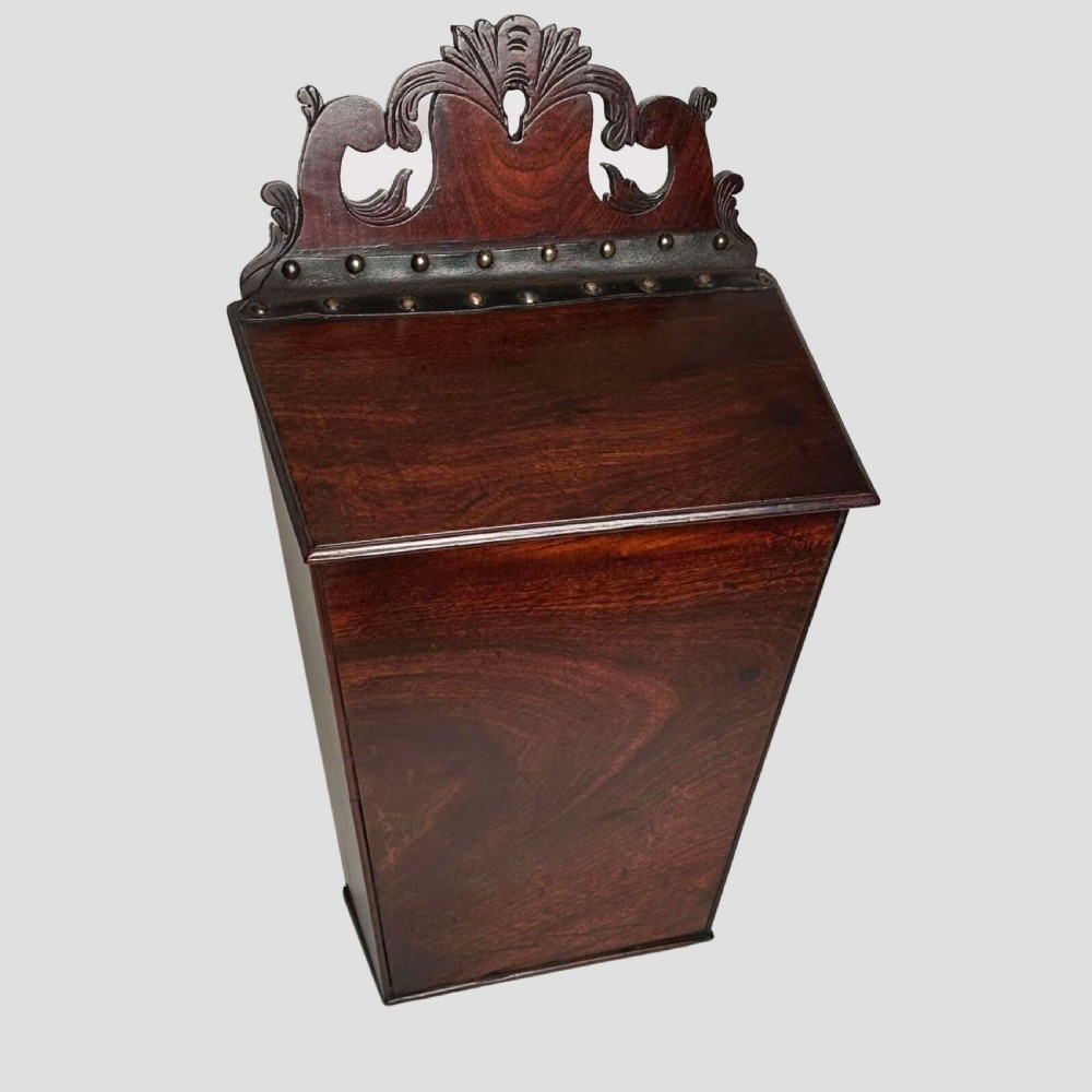 A Georgian mahogany wall-hanging cutlery box with a sloped lid, brass stud details, and a carved pierced crest. View II