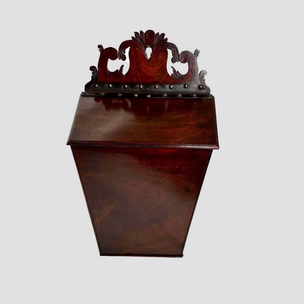 A Georgian mahogany wall-hanging cutlery box with a sloped lid, brass stud details, and a carved pierced crest. View IV