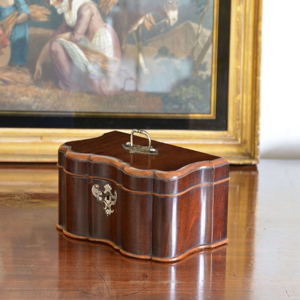 An early 18th-century shaped red walnut tea caddy featuring a top brass handle and a metal escutcheon with a key inserted.