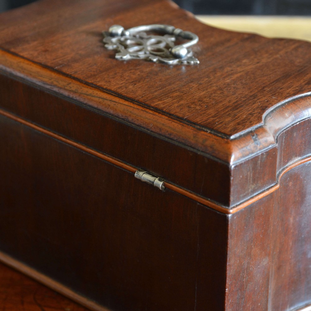 An early 18th-century shaped red walnut tea caddy featuring a top brass handle and a metal escutcheon with a key inserted. View V