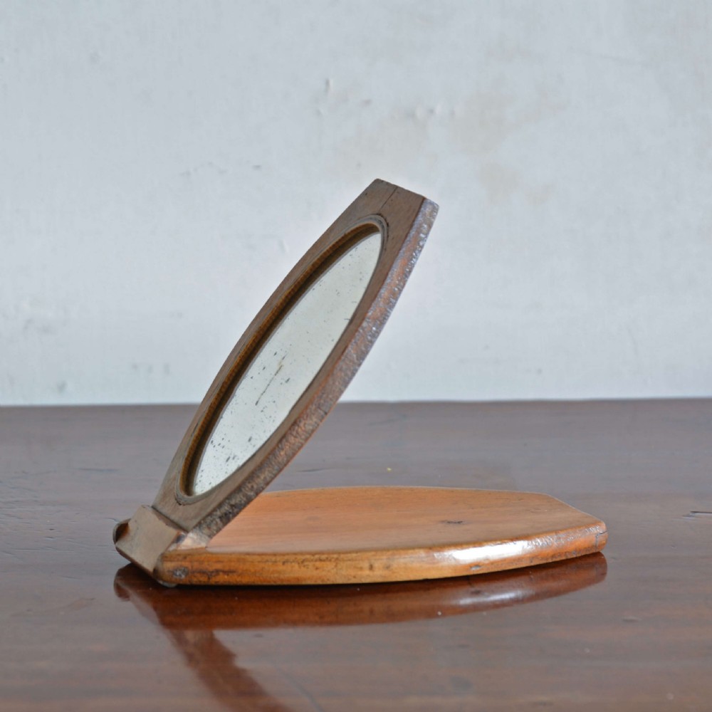 A hinged walnut campaign shaving mirror with an oval glass plate resting open on a wooden surface. View II