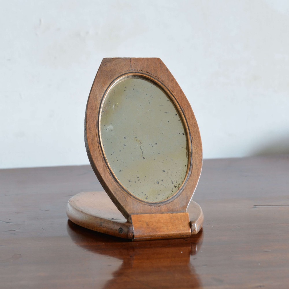 A hinged walnut campaign shaving mirror with an oval glass plate resting open on a wooden surface. View III