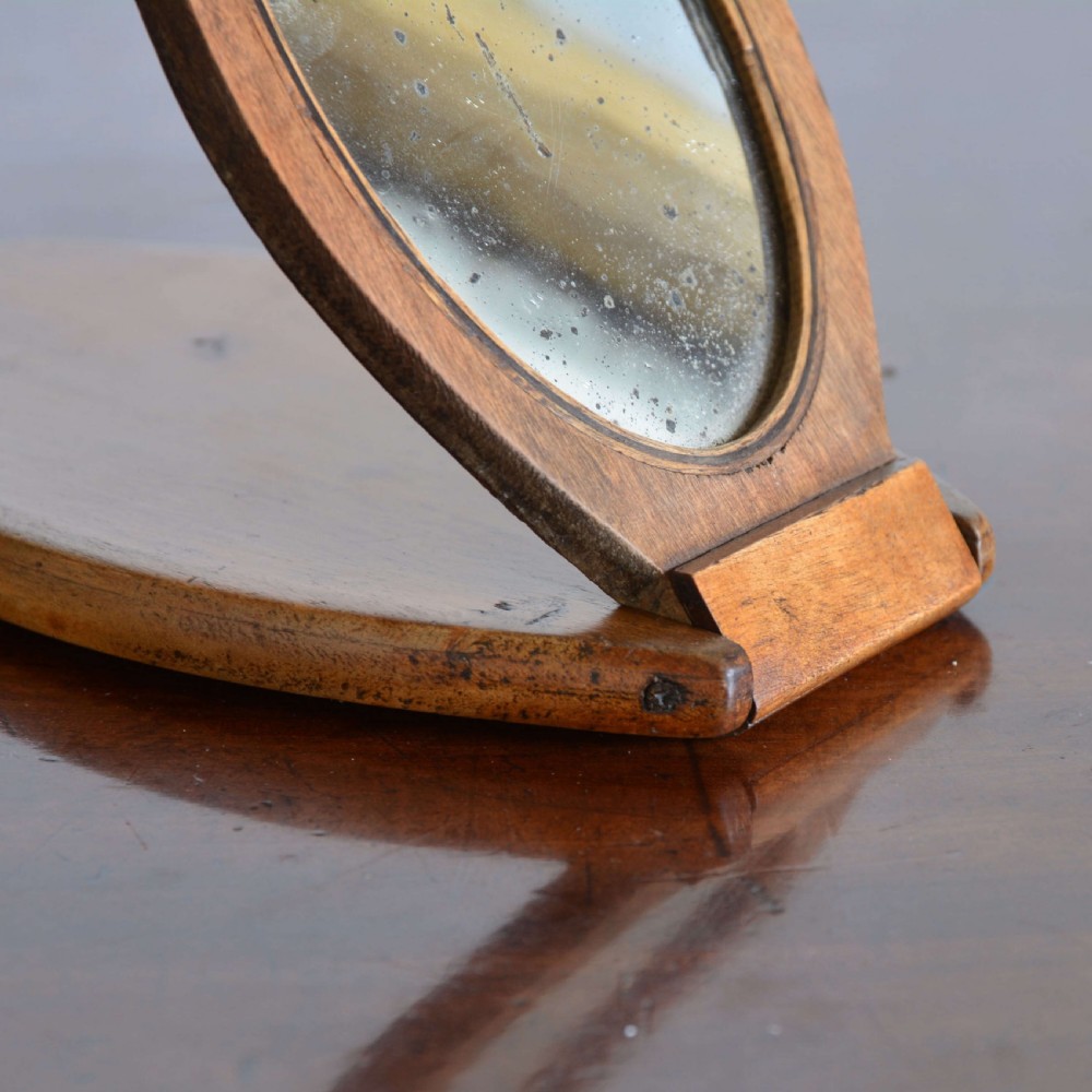 A hinged walnut campaign shaving mirror with an oval glass plate resting open on a wooden surface. View IV