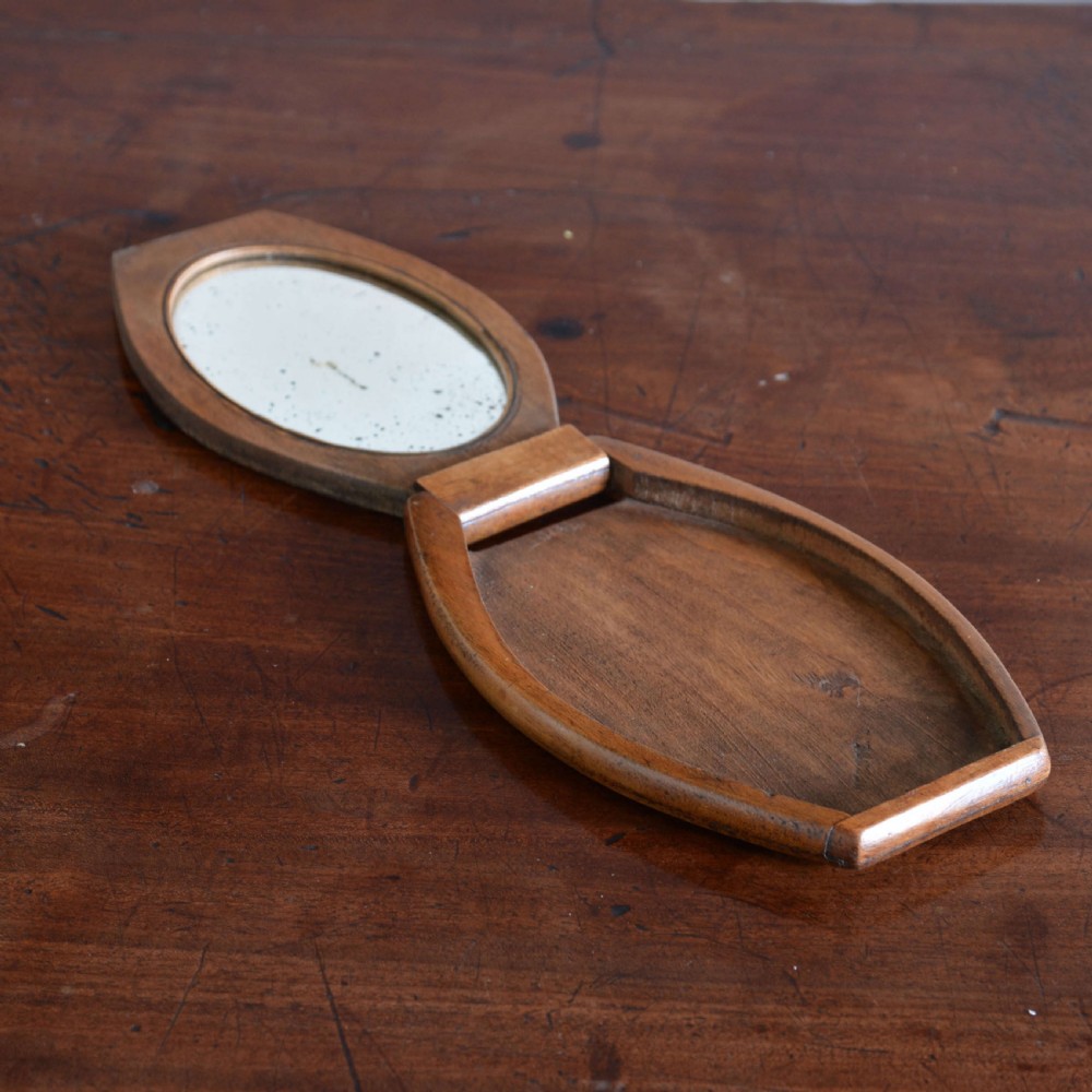 A hinged walnut campaign shaving mirror with an oval glass plate resting open on a wooden surface. View VI