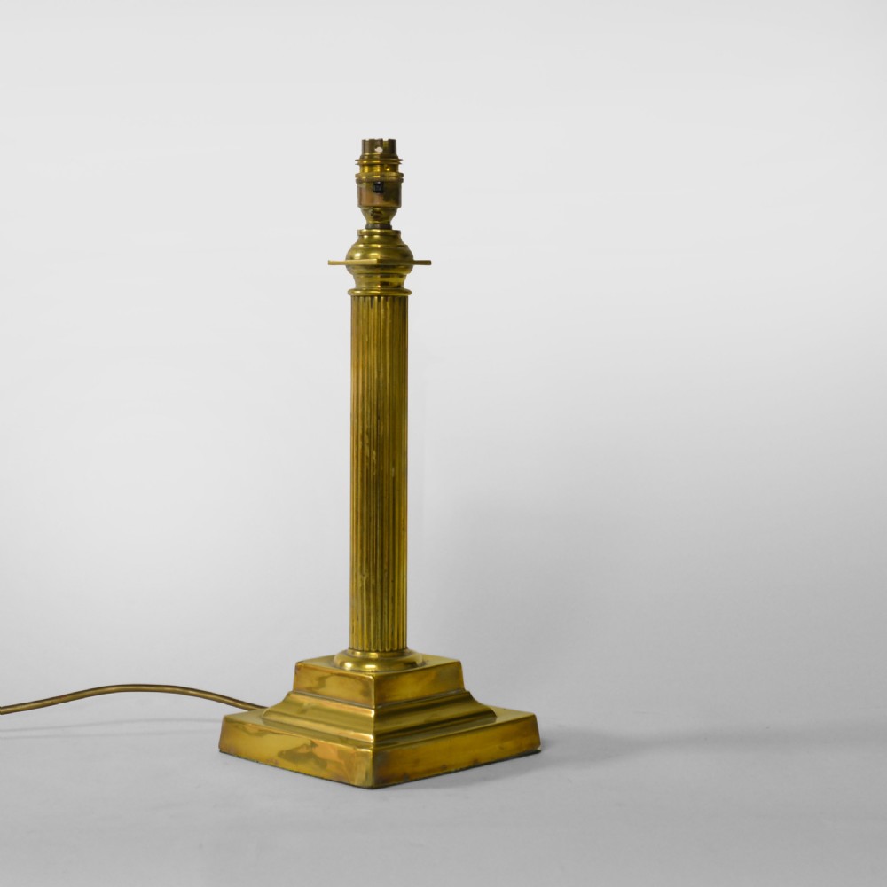 A fluted brass column table lamp base standing on a stepped square pedestal base.