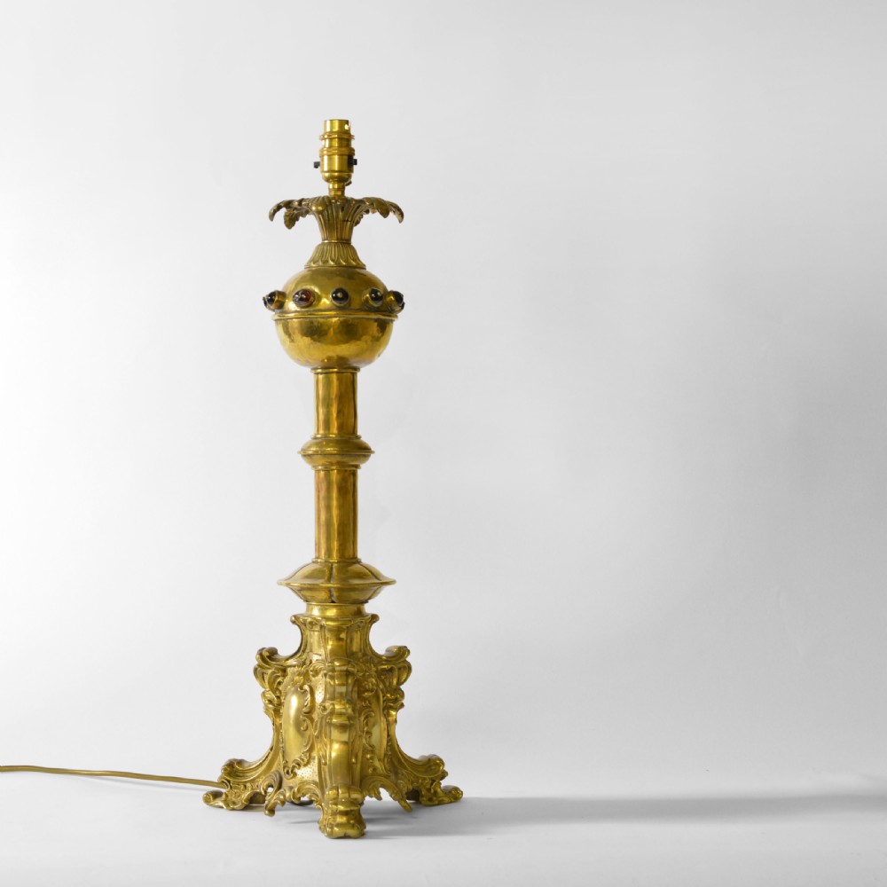 An ornate brass table lamp crafted in a French Gothic style featuring a scrollwork base, turned column, and a central spherical knop set with dark red cabochon accents.