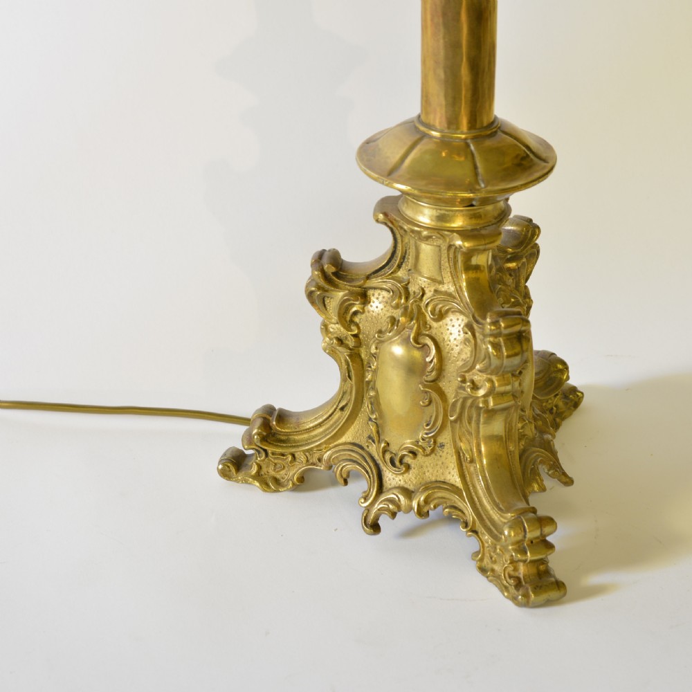 An ornate brass table lamp crafted in a French Gothic style featuring a scrollwork base, turned column, and a central spherical knop set with dark red cabochon accents. View V