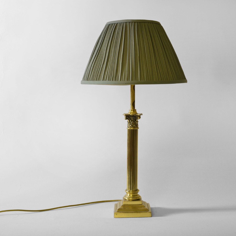 A Victorian brass table lamp designed as a fluted Corinthian column with a stepped base, topped with a pleated sage green fabric shade.