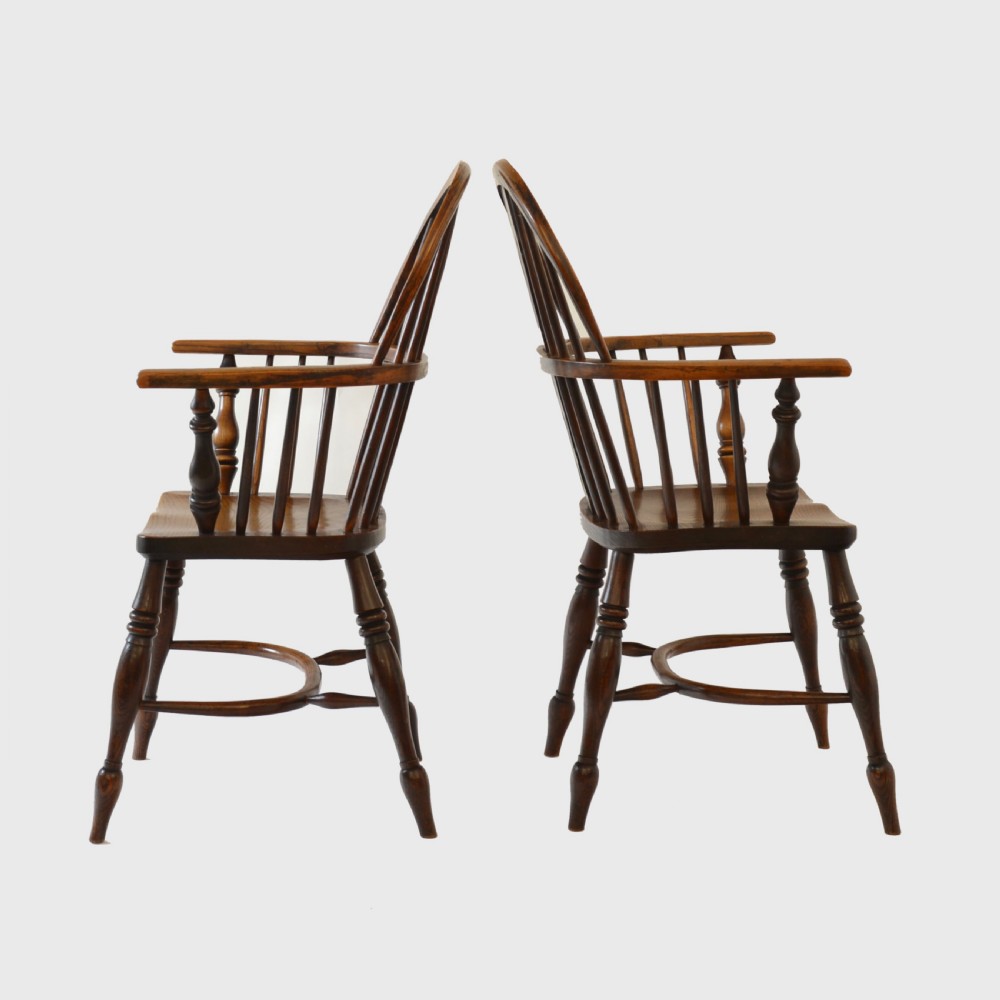 A pair of warm brown wooden Windsor armchairs featuring hoop backs, central pierced splats, turned legs, and curved stretchers. View V