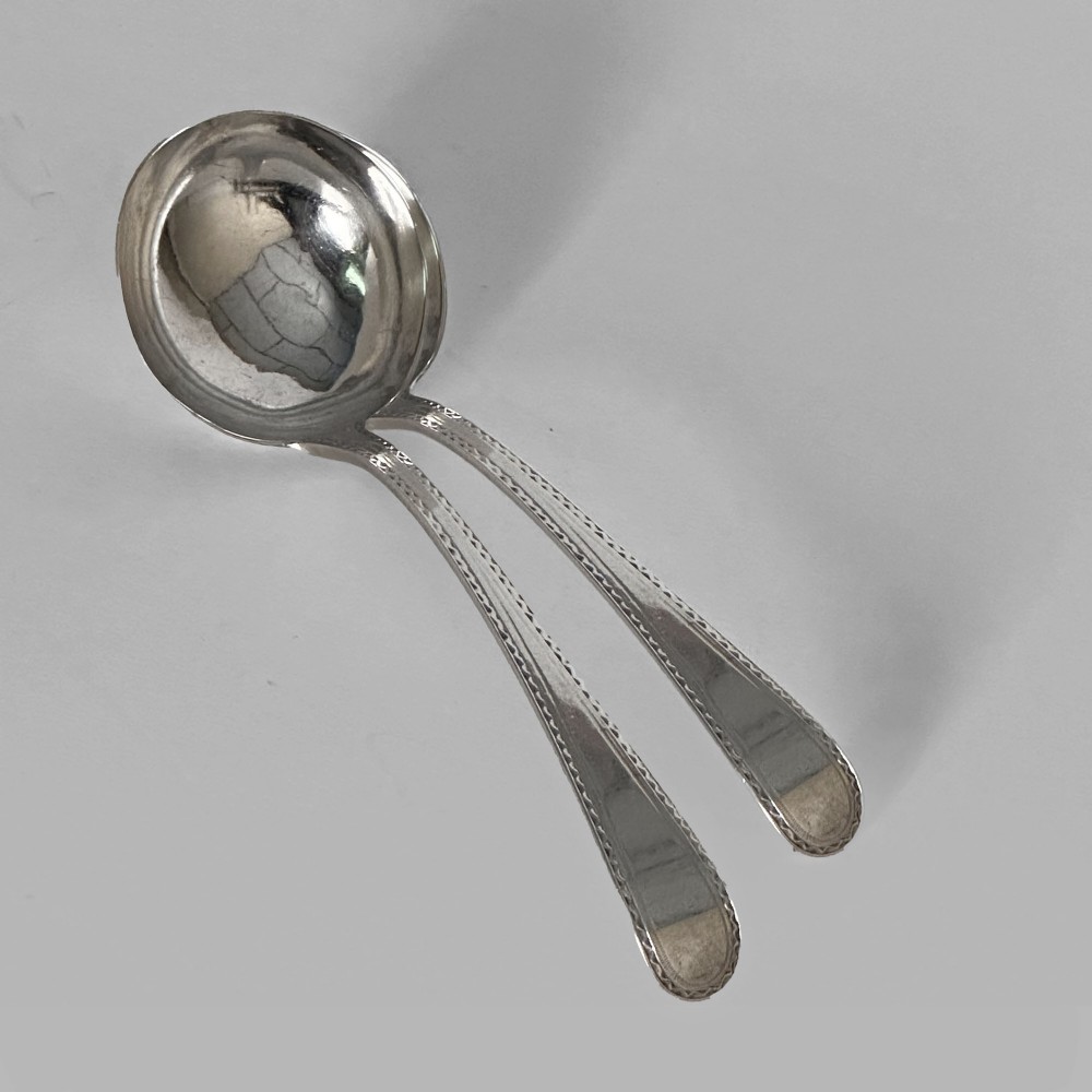 A pair of Georgian sterling silver sauce ladles with circular bowls and beaded edge decoration along the handles.