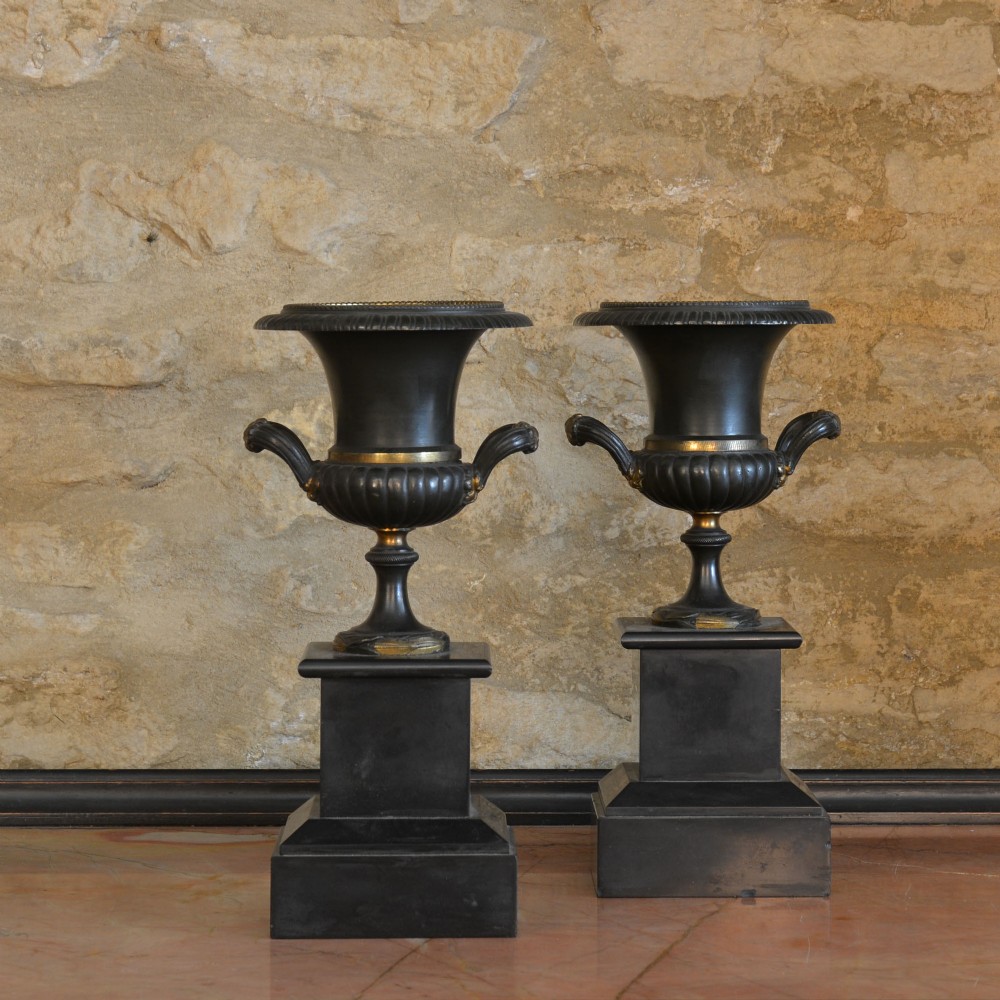 A pair of dark patinated bronze Campana-form urns with gilded ormolu details set upon square black plinths.