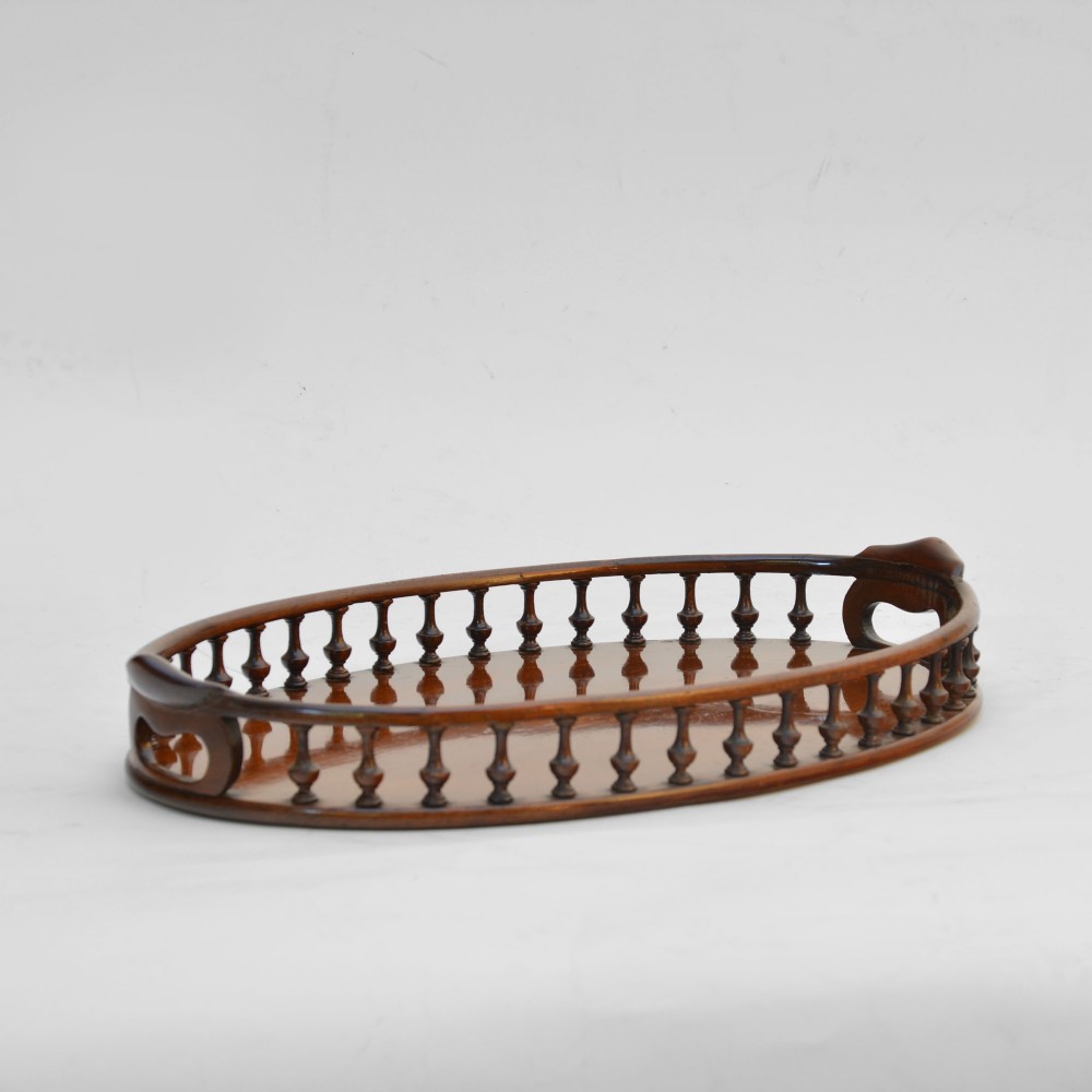 An oval mahogany tray featuring a raised turned spindle gallery around the perimeter and integrated carved carrying handles.