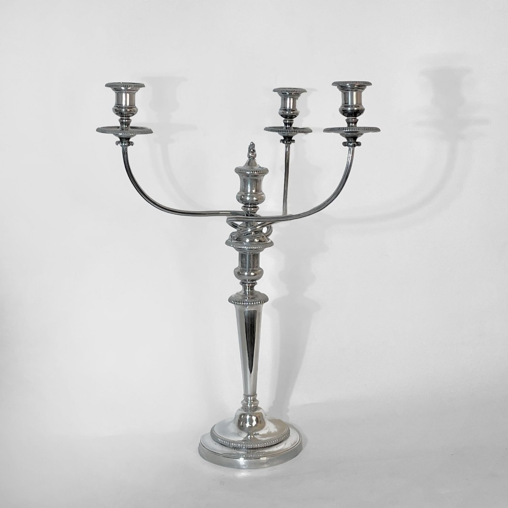 A silver-plated Regency three-light candelabrum featuring reeded curved branches, beaded rims, and a tapered central column resting on a circular stepped base.