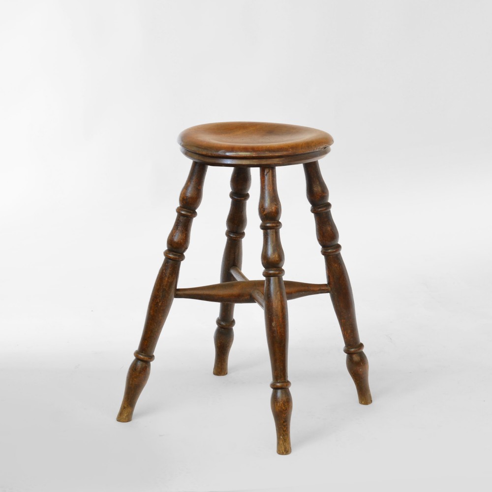 A 19th-century dark brown turned sycamore pub stool featuring four splayed turned legs, a dished circular seat, and cross-stretchers.