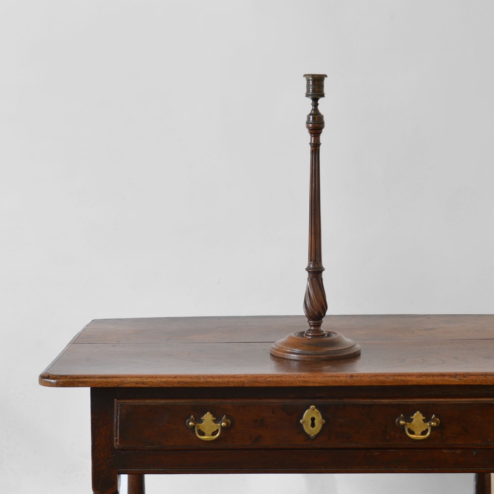A tall Georgian turned mahogany candlestick featuring a fluted and spiral-carved stem resting on a stepped circular base with a brass sconce.
