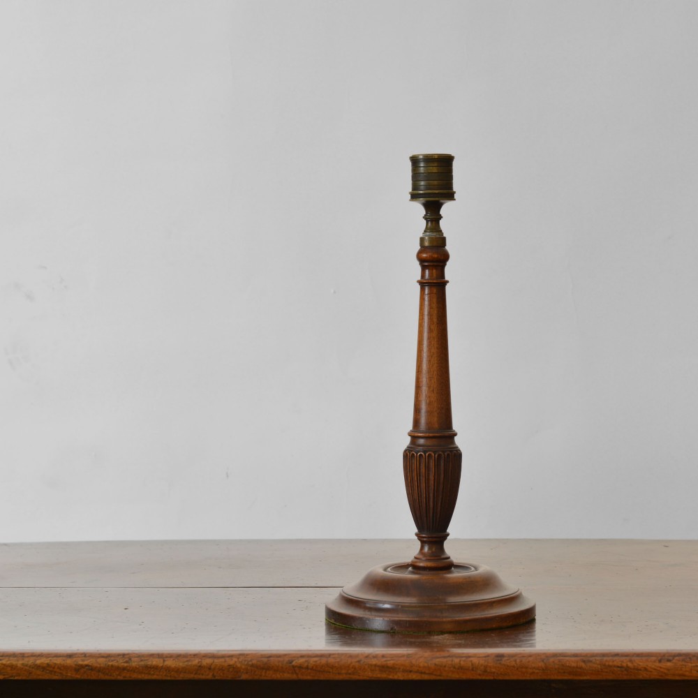 A tall turned mahogany candlestick with fluted column detailing, a brass nozzle insert, and a wide moulded circular base.