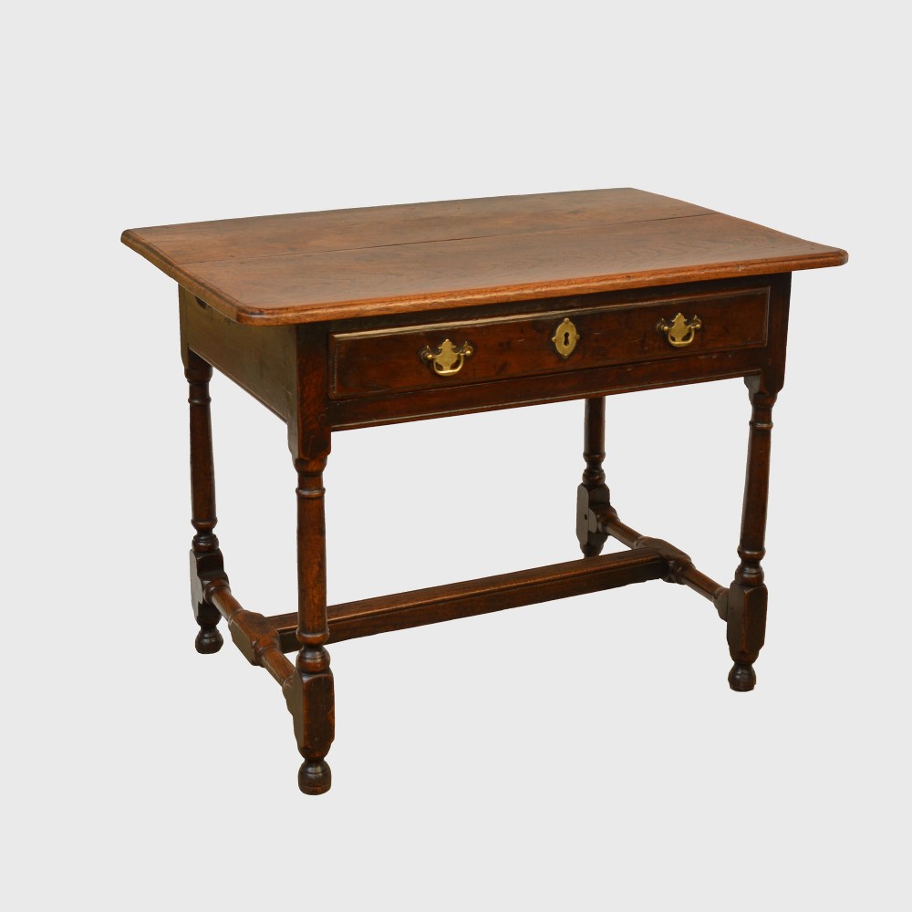 An 18th-century side table made from dark warm-toned wood with a single drawer, brass handles, and turned legs joined by stretchers.