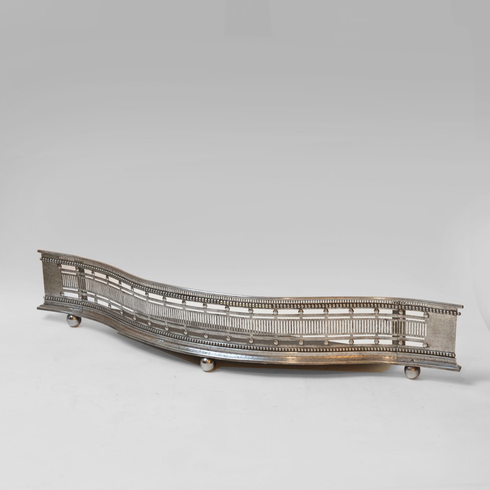 A Georgian steel bowfront fireplace fender featuring pierced geometric fretwork, beaded rim details, and three spherical ball feet.