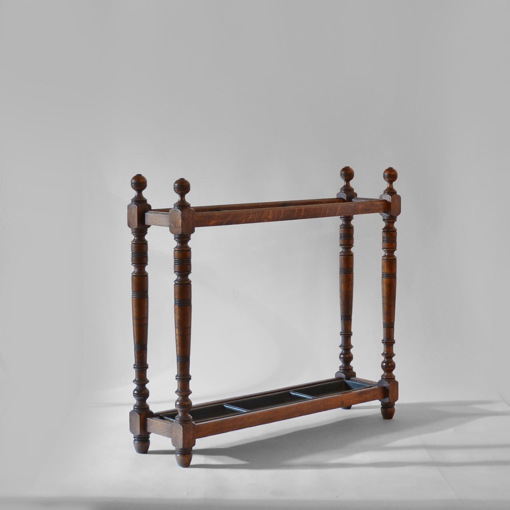 A dark oak umbrella stand featuring turned posts, spherical finials, and an integrated metal drip tray at the base.
