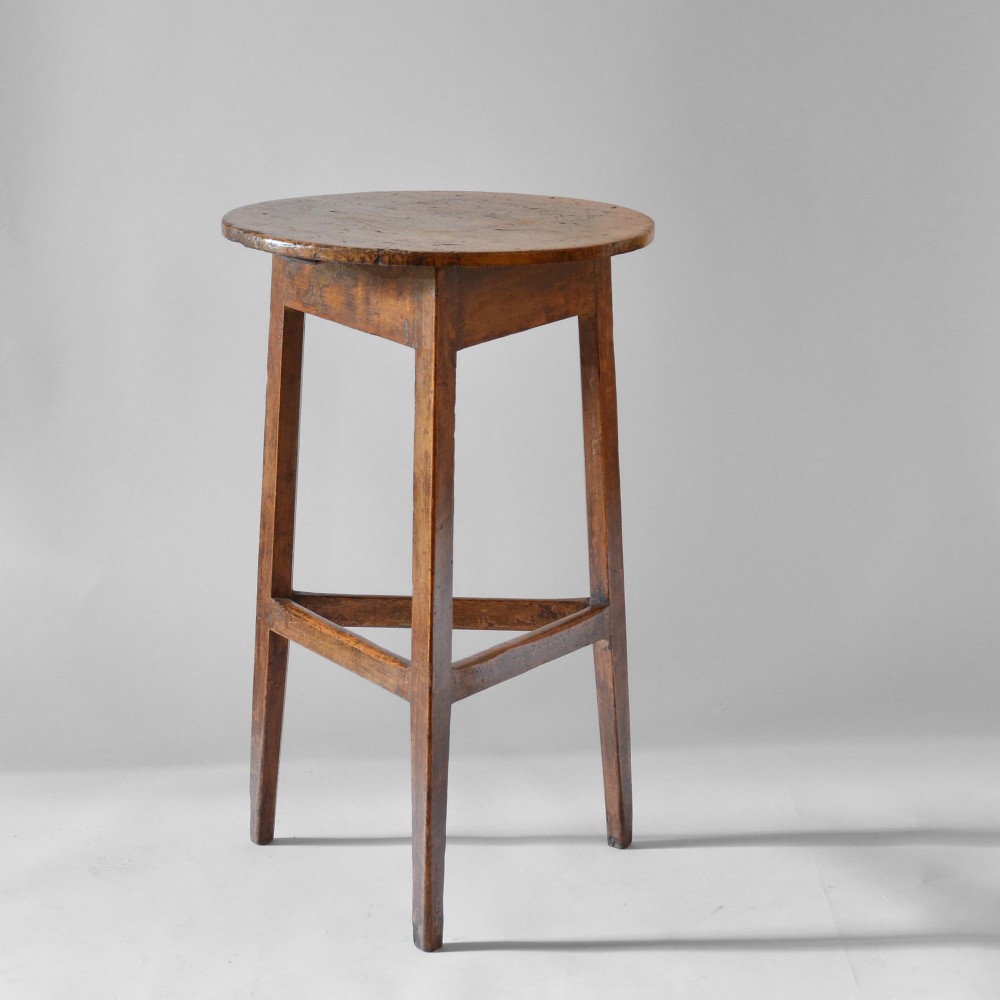 A Georgian vernacular pine cricket table featuring a circular top supported by three legs with a lower triangular stretcher.
