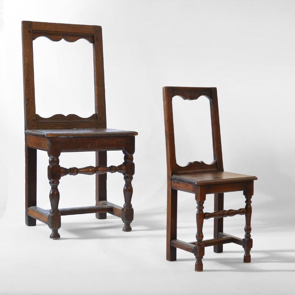 A small, warm brown antique fruitwood child chair featuring an open rectangular back with contoured cut-outs, a solid seat, and turned front legs with stretchers. View II