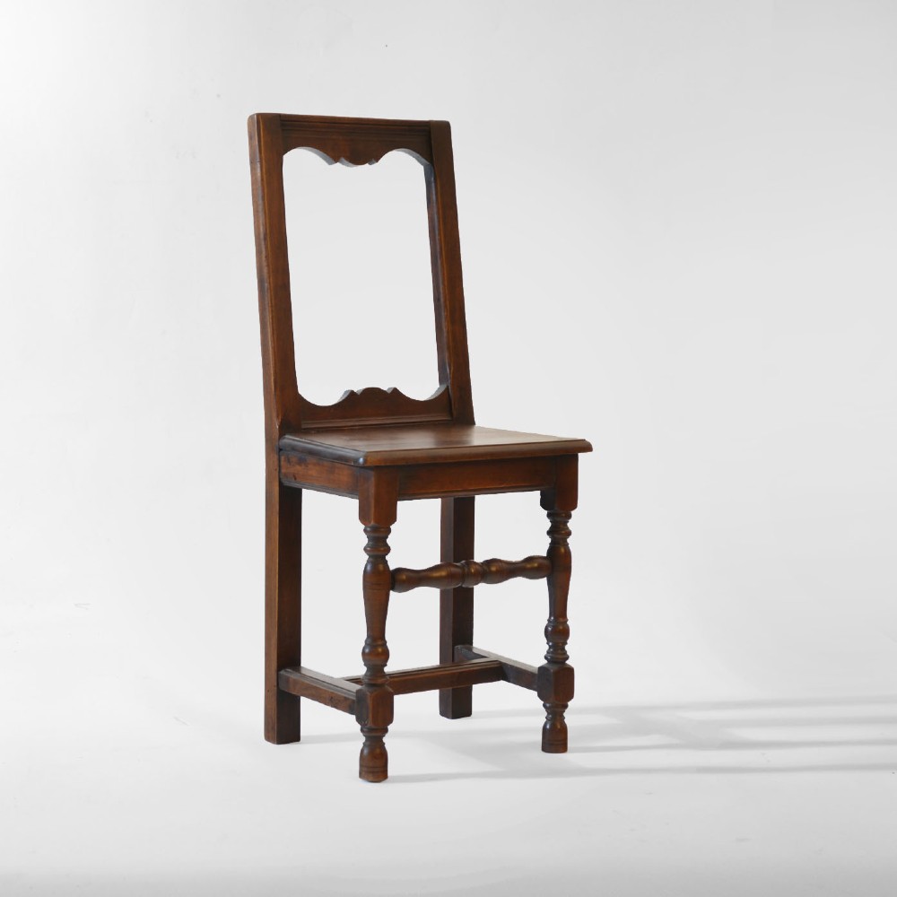 A small, warm brown antique fruitwood child chair featuring an open rectangular back with contoured cut-outs, a solid seat, and turned front legs with stretchers. View III