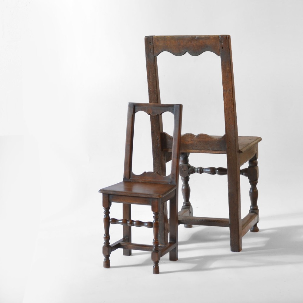 A small, warm brown antique fruitwood child chair featuring an open rectangular back with contoured cut-outs, a solid seat, and turned front legs with stretchers. View IV