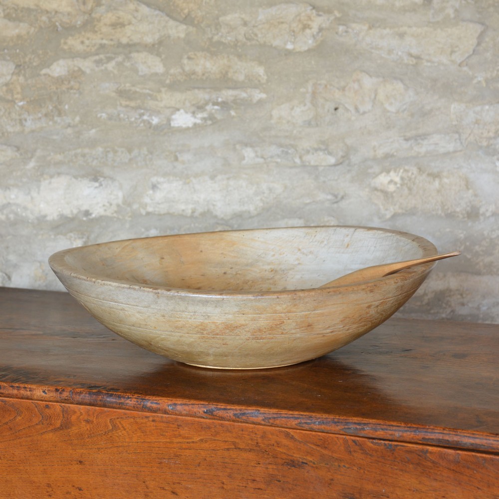 A large hand-turned pale sycamore wooden dairy bowl containing a single carved wooden spoon.