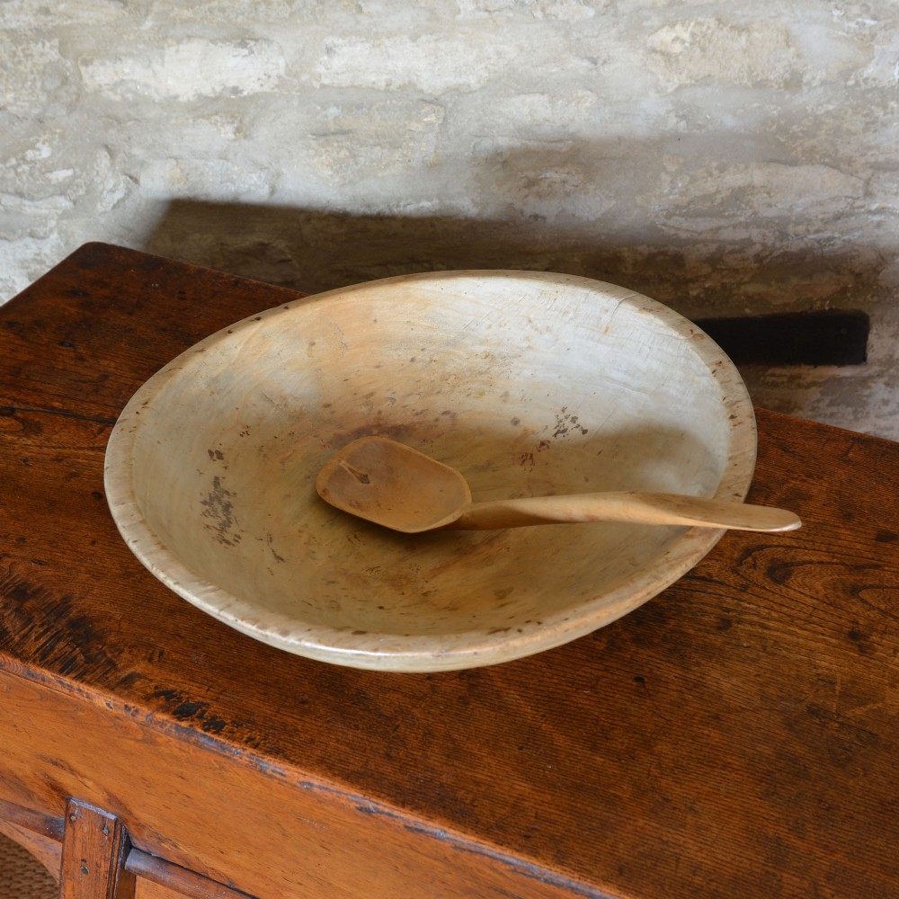 A large hand-turned pale sycamore wooden dairy bowl containing a single carved wooden spoon. View II