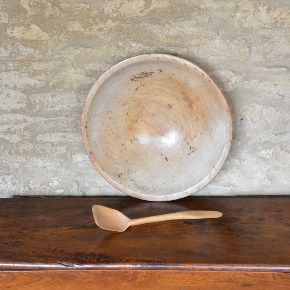 A large hand-turned pale sycamore wooden dairy bowl containing a single carved wooden spoon. View III