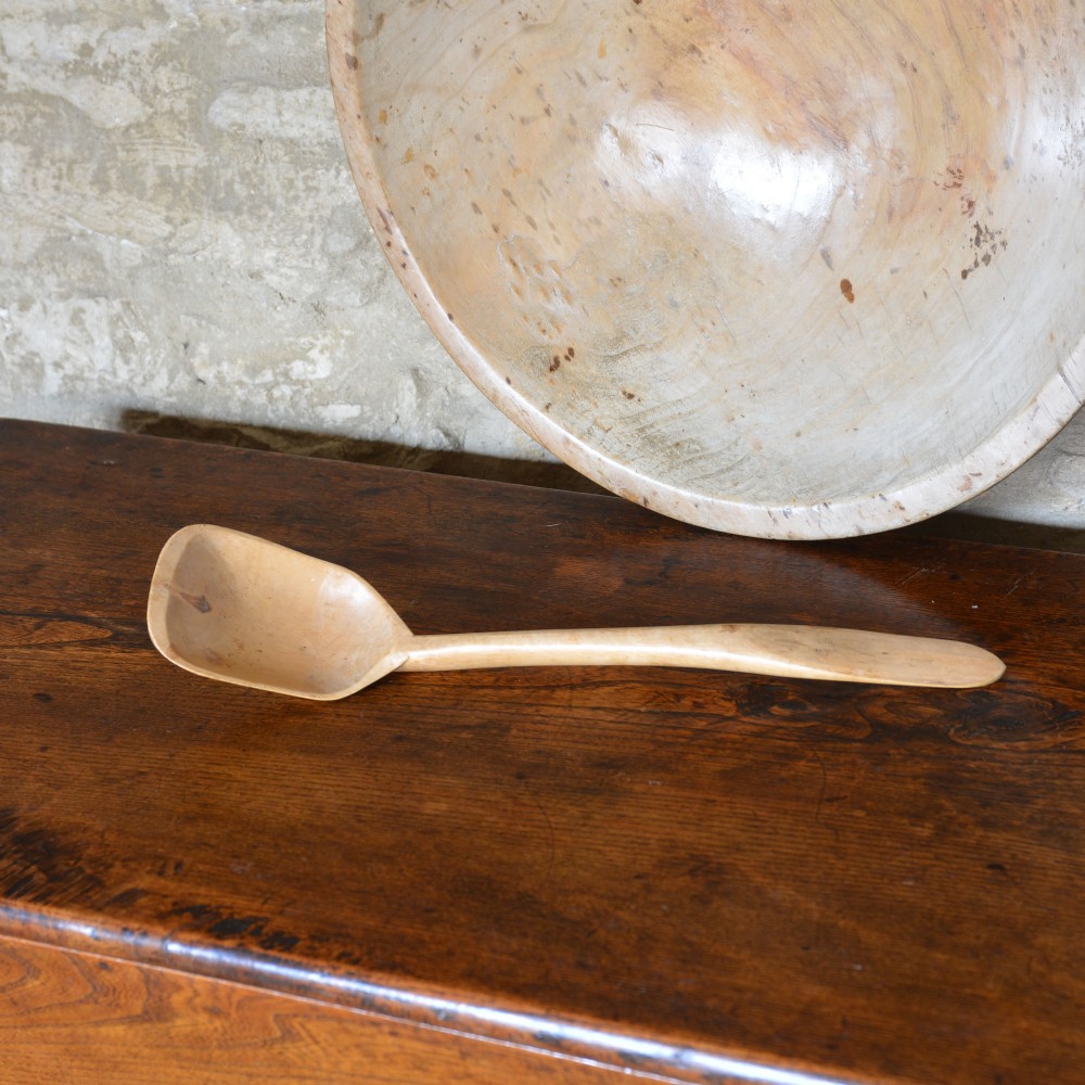 A large hand-turned pale sycamore wooden dairy bowl containing a single carved wooden spoon. View IV