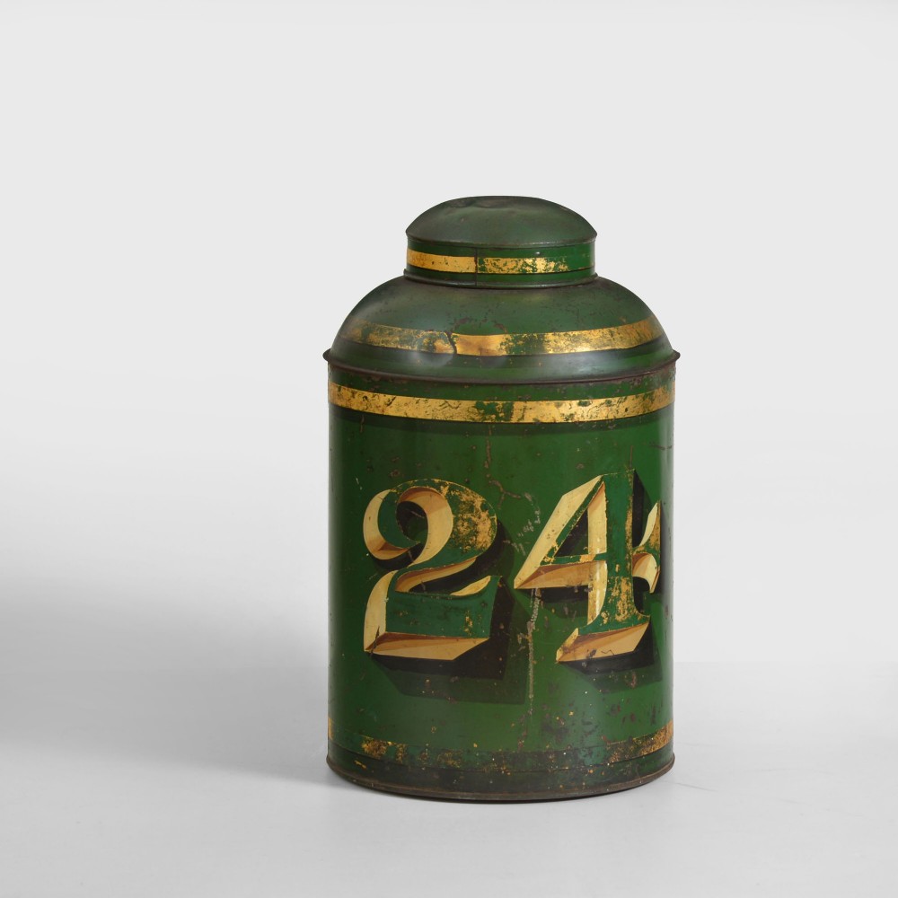A cylindrical dark green antique tin tea canister featuring gilded bands and a prominent hand-painted number 24 on the front.