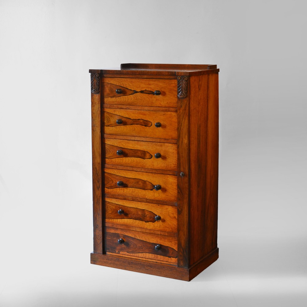 A 19th-century rosewood Wellington chest featuring six graduated drawers, turned wooden knobs, carved corbels, and a side-locking bar on a plinth base.