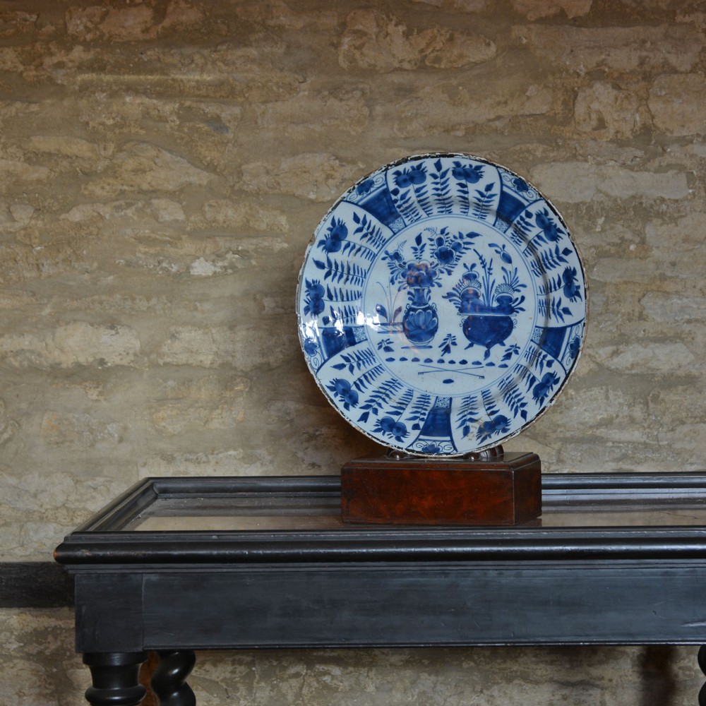 A circular tin-glazed earthenware charger featuring hand-painted cobalt blue urn and botanical motifs on a white background with a panelled rim. View II