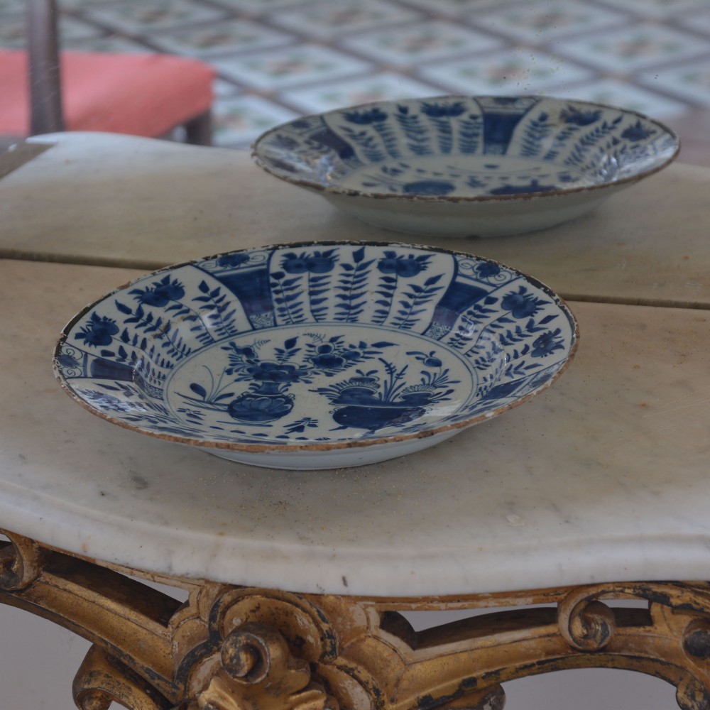 A circular tin-glazed earthenware charger featuring hand-painted cobalt blue urn and botanical motifs on a white background with a panelled rim. View III