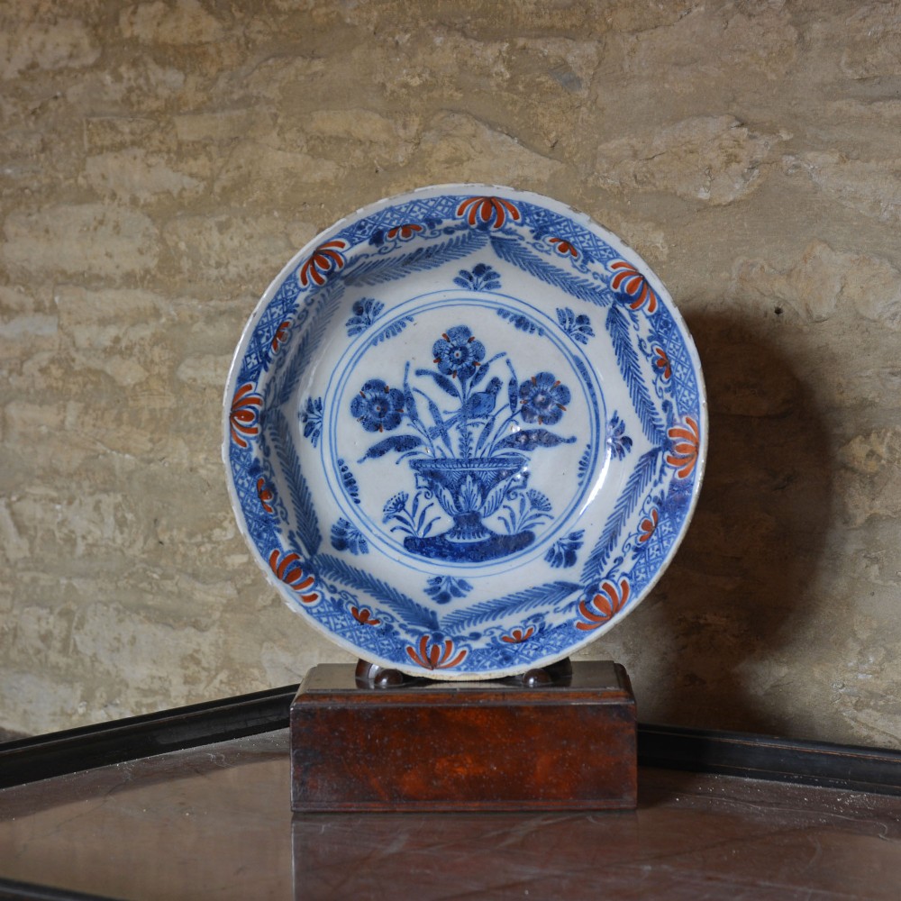 A circular 18th-century tin-glazed Delftware shallow bowl featuring hand-painted cobalt blue floral motifs and iron-red accents.